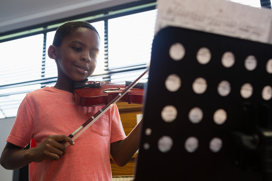 微笑的男孩站在教室里拉小提琴