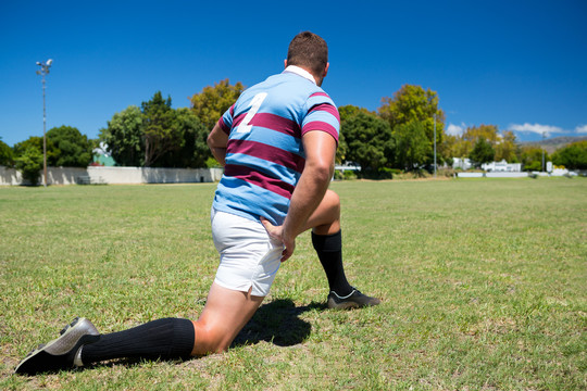 橄榄球运动员跪在蓝天草地上锻炼