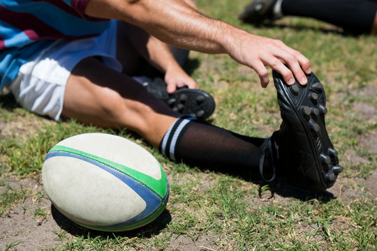 橄榄球运动员坐在草地上触摸脚趾