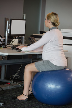 孕妇在健身球上在办公室工作