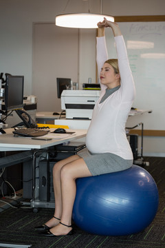 孕妇在办公室健身球上做伸展运动