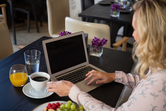 女商人拿着咖啡杯在餐厅使用电脑