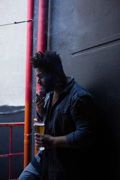 在酒吧门口喝啤酒时抽烟的男人