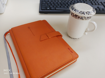 办公桌上的黄皮笔记本和白瓷茶杯