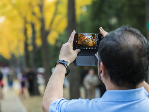 用手机拍摄秋景的男人