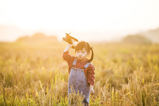 小女孩拿着飞机玩具在田野玩耍
