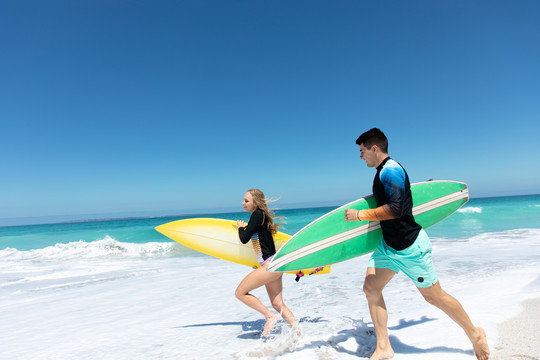 一对夫妇举着冲浪板在海滩上奔跑