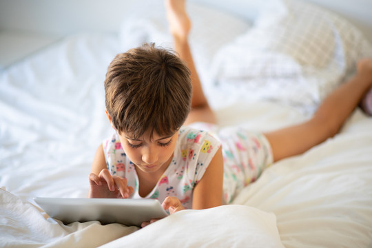 小女孩在床上玩数码平板电脑