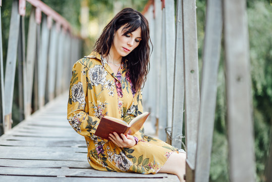 在乡村桥上看书的年轻女子。