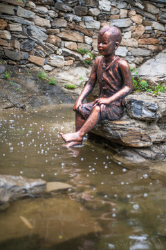 乡村小溪边戏水的少年铜像