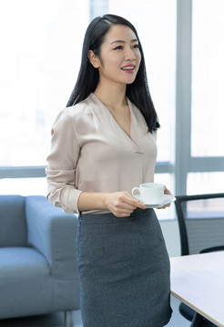 年轻商务女士在办公室喝咖啡