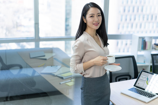 年轻商务女士在办公室喝咖啡