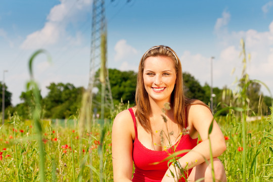 身着红色t恤的妇女站在蓝天下的草地或麦田里，背景是一根电线杆