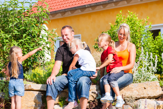 一个年轻的家庭在家或房子前面，三个孩子坐在阳光下