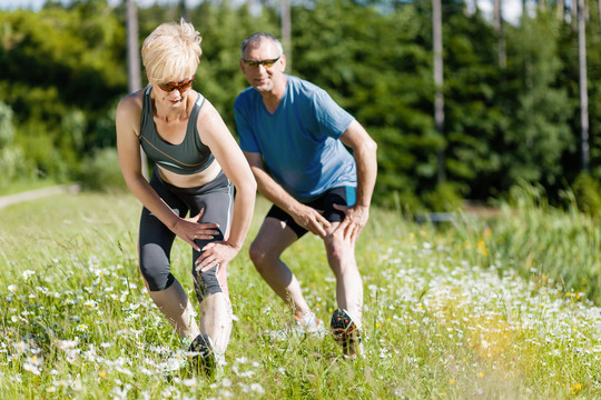 穿慢跑服的老年夫妇在户外做运动和体育锻炼，做伸展运动和体操