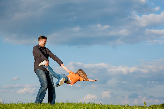 父亲和他的小女儿在草地上玩耍，他把她扔来扔去