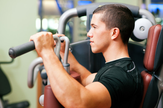 在健身房里，男子在蝶泳机上进行举重健身训练