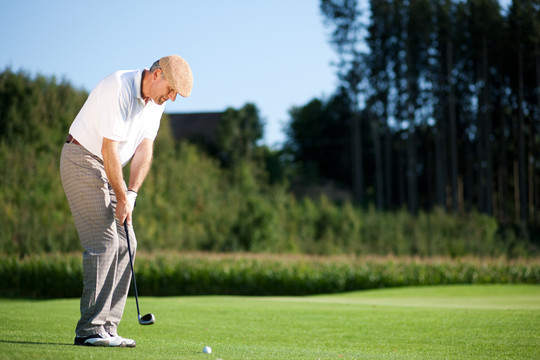 一位高级高尔夫球手正在打高尔夫球，他正在一个美妙的夏日午后打球