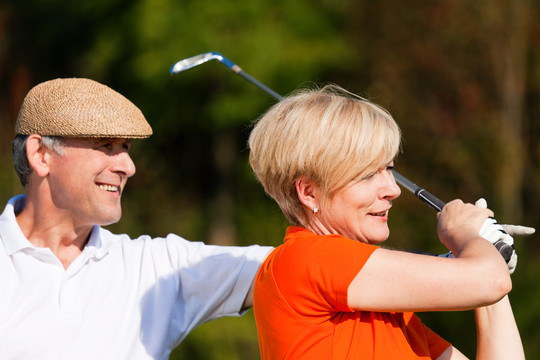 一对老年夫妇在夏天的下午打高尔夫球，男搭档是女高尔夫球手的教练