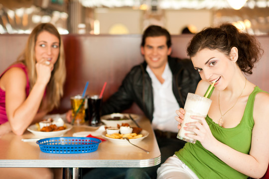 三个朋友在一家餐厅或小餐馆吃薯条和喝奶昔，镜头可用光，非常有选择性的重点