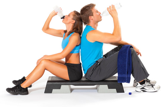 一对积极运动的夫妇背靠背坐在有氧踏步机上，在白色背景下运动后从瓶子里喝水