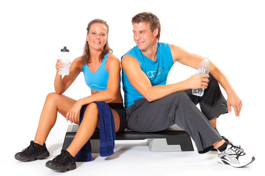 一对白人男子和一对妇女坐在有氧踏步机上，一边休息，一边在剧烈运动后拿着水瓶