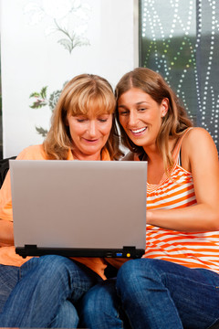 女儿在家里给妈妈解释上网，两个女人都坐在笔记本电脑前