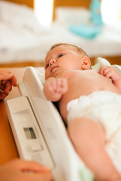 婴儿在体重秤上，母亲或医生正在检查新生儿的健康和发育情况