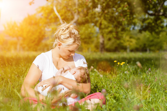 在一个阳光明媚的日子里，母亲在草地上给孩子喂奶
