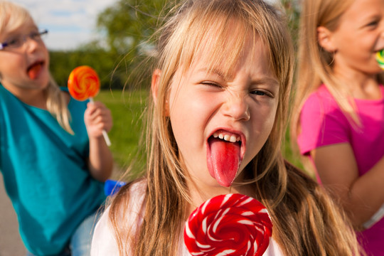 三个女孩在吃棒棒糖，前面的女孩伸出舌头