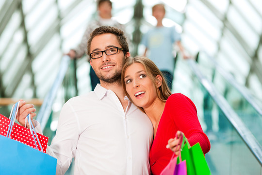 一对男女在购物中心的自动扶梯上提着五颜六色的袋子