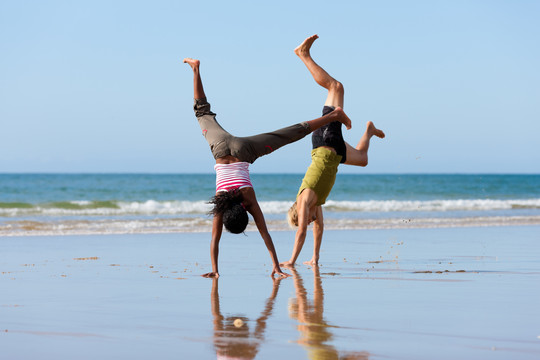 一对年轻的体育情侣——白人男子和非裔美国女子——在沙滩上做体操