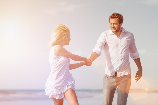 一对穿着白色衣服的情侣在沙滩上跑来跑去度假或度蜜月