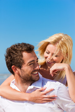 一对相爱的白种人在海滩上的蓝天下背着他的女人