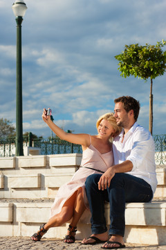 一对夏天在城里度假的夫妇坐在砖墙上晒太阳，画画