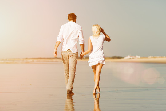 一对穿着白色衣服的情侣在沙滩上散步，他们可能正在度假甚至度蜜月