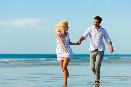 一对穿着白色衣服的情侣在沙滩上跑了下来，他们可能正在度假甚至度蜜月