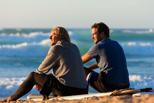 两个冲浪者坐在沙滩上的冲浪板上讨论海浪