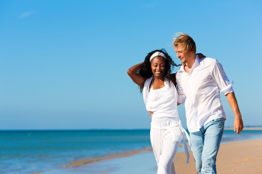 一对幸福的夫妇——黑人女人和白人男人——度假时在海滩上散步和跑步