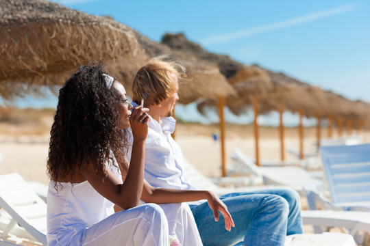 一对夫妇坐在沙滩上晒太阳的椅子上抽烟