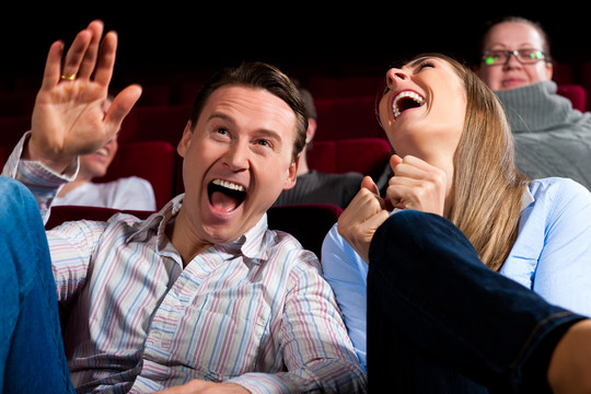夫妻和其他人，可能是朋友，在电影院看电影，似乎是一部有趣的电影