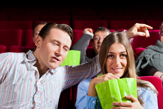 一对夫妇在电影院看电影，他们在吃爆米花