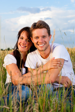 一对幸福的夫妇坐在草地上或麦田里，在夏天互相拥抱