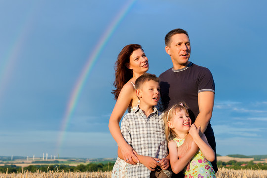 幸福的家庭——母亲、父亲、孩子们——站在夏日的彩虹下，展望美好的未来