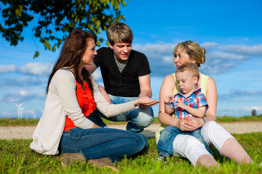 家庭-祖母，母亲，父亲和孩子坐在花园里玩耍