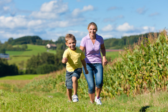 在一个美丽的夏日，快乐的家庭在草地上奔跑——母亲正试图抓住她的儿子