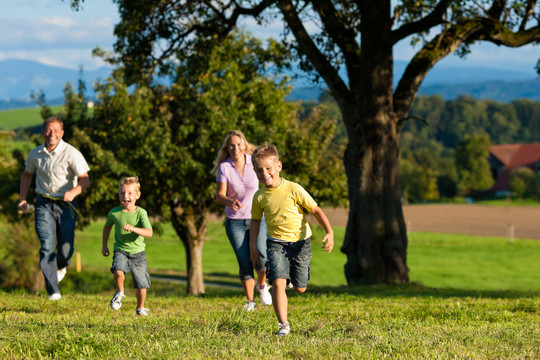 在一个美丽的夏日，快乐的户外家庭在草地上奔跑——他们试图抓住对方