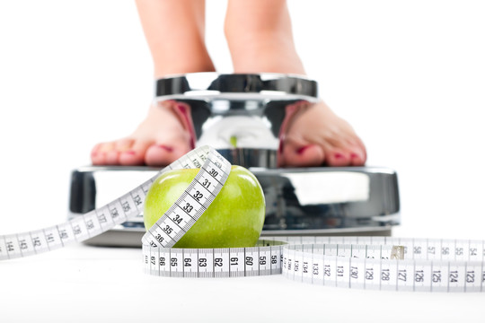 饮食和体重，年轻女子站在秤上，只看到脚，一个苹果和一个卷尺