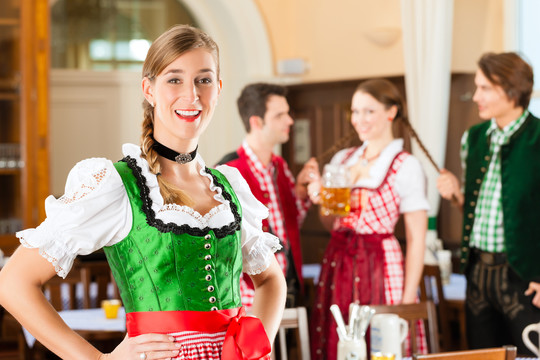 年轻人在传统的巴伐利亚餐馆或酒吧里，一个女人站在前面，一群人在后面