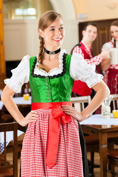 年轻人在传统的巴伐利亚餐馆或酒吧里，一个女人站在前面，一群人在后面